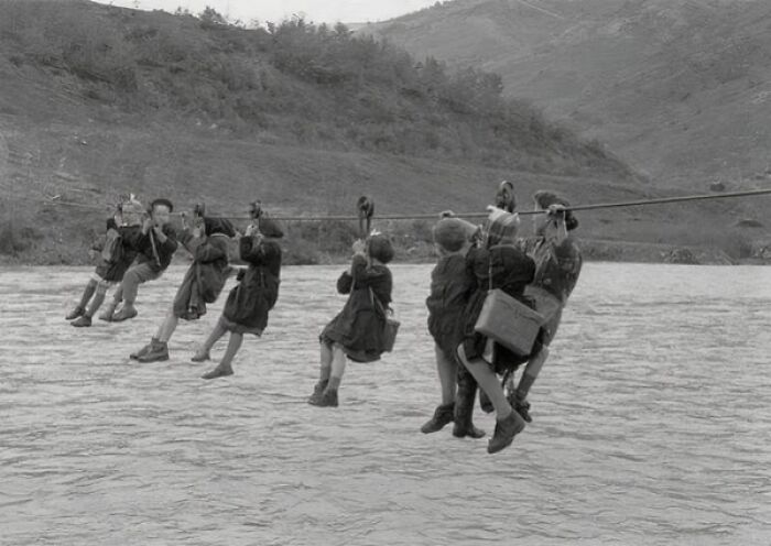 Children crossing a river on a rope pulley system in an old black and white photo from unique old photos collection.