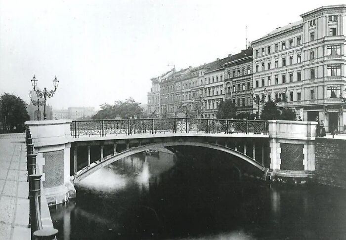 Black and white historical photograph of a 100-year-old city bridge and riverside buildings from the past.