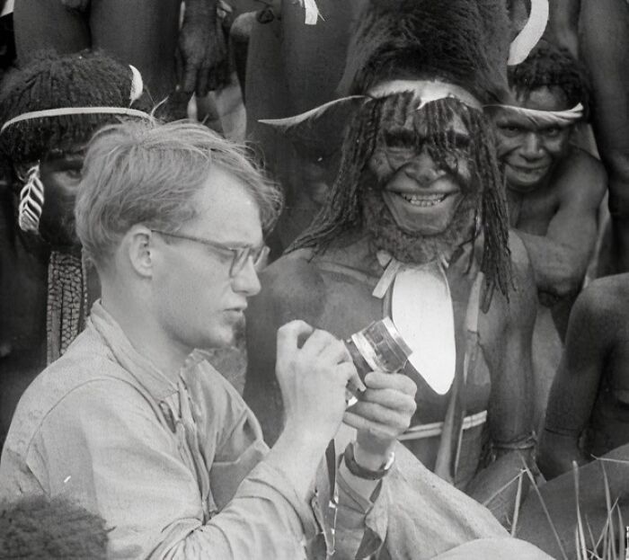 Black and white unique old photo showing a man examining an object surrounded by tribal people in traditional attire.