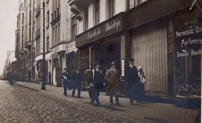 Early 20th-century street scene with men walking on cobblestone road in historical photographs showing the world 100 years ago.