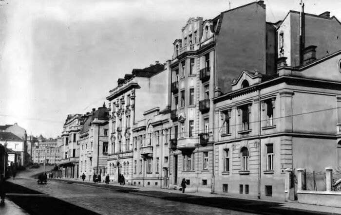 Black and white historical photograph of a city street with early 20th-century architecture and few pedestrians 100 years ago