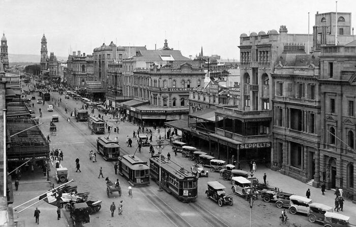 Busy city street scene with early 20th-century cars, trams, and pedestrians, historical photographs showing the world 100 years ago