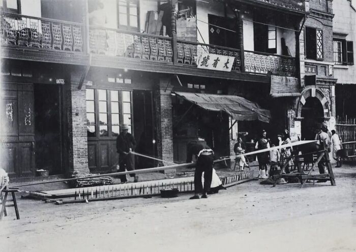 Black and white historical photograph showing street life and traditional activities from 100 years ago.