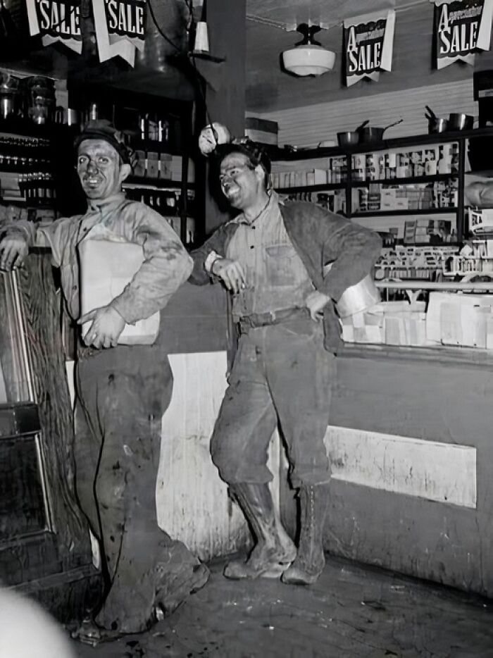 Two miners covered in dirt inside a store, captured in a unique old photo showing their daily life and work environment.