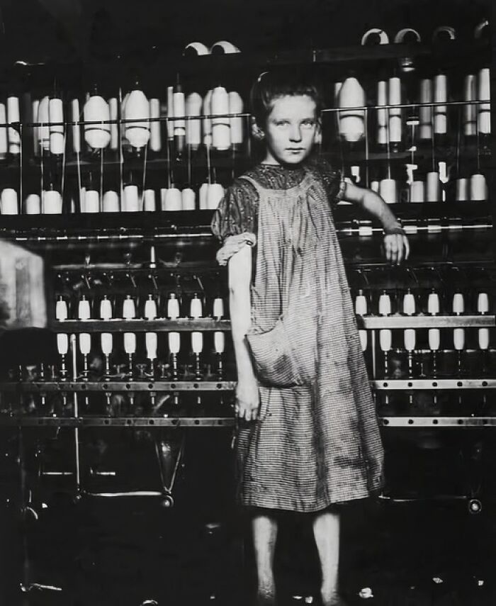 Young girl working in textile factory surrounded by spools, a unique old photo capturing early industrial labor conditions.