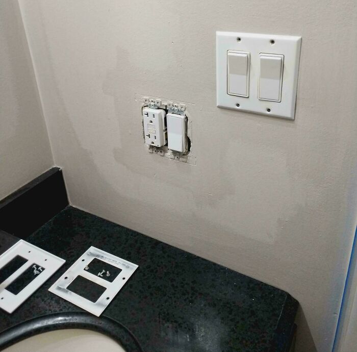 Partially installed light switch and outlet on bathroom wall showing real-life glitches in the matrix with missing faceplates.