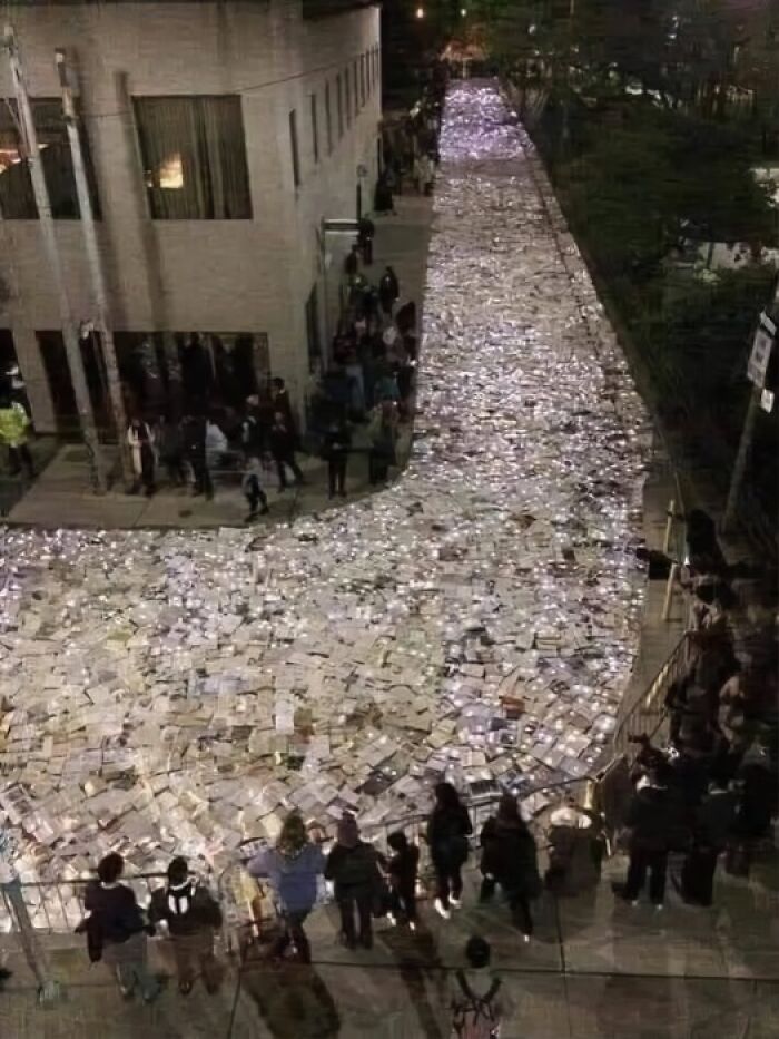 Outdoor nighttime event with a large crowd surrounding a river of illuminated books showcasing the wonderful world.