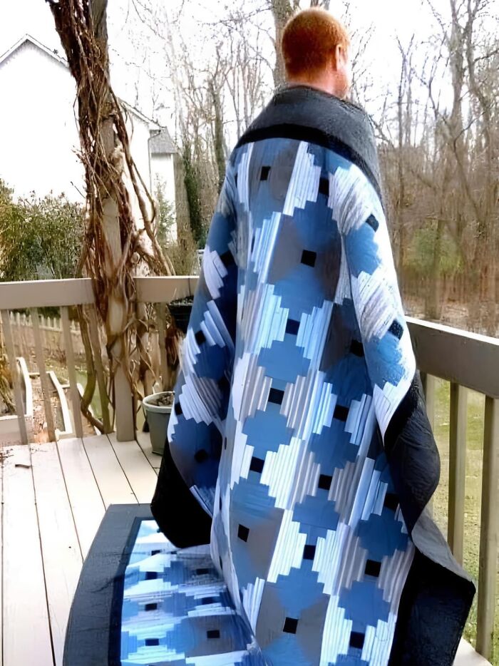 Person wrapped in a blue and white patterned quilt on a porch overlooking a wooded backyard in the wonderful world.
