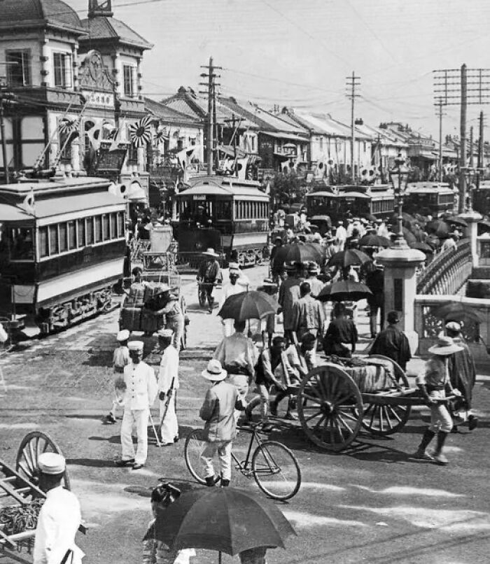 Crowded street scene with trams, pedestrians, and carts in a historical photograph showing the world 100 years ago.