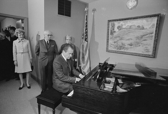 Richard Nixon playing piano while people watch in a rare and interesting historical photograph from a private setting.
