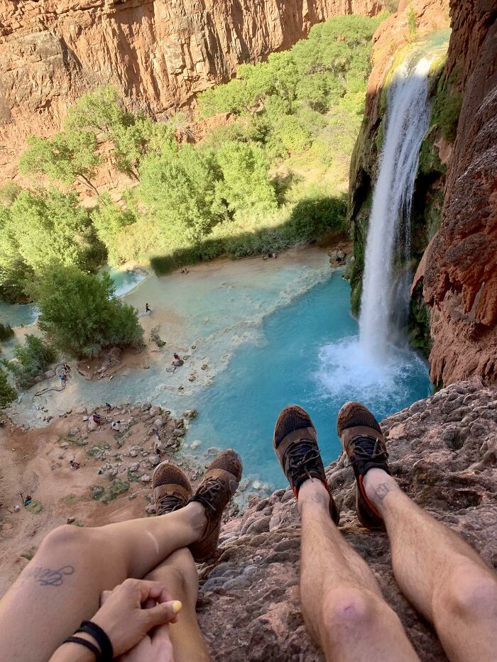 Two people sitting on a cliff above a turquoise pool and waterfall, capturing amazing moments of unbelievable luck.