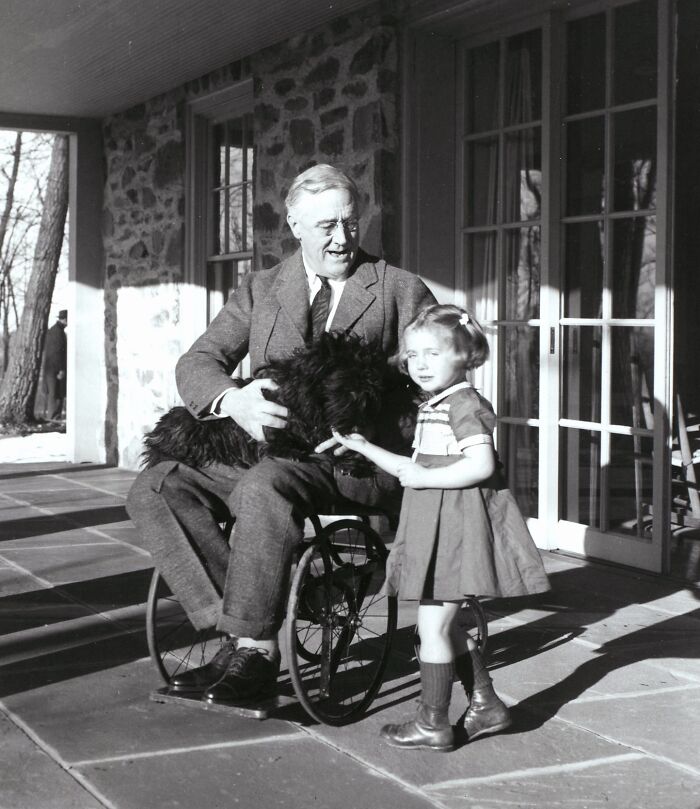 Rare historical photograph of a man in a wheelchair with a young girl and a black dog on a porch.