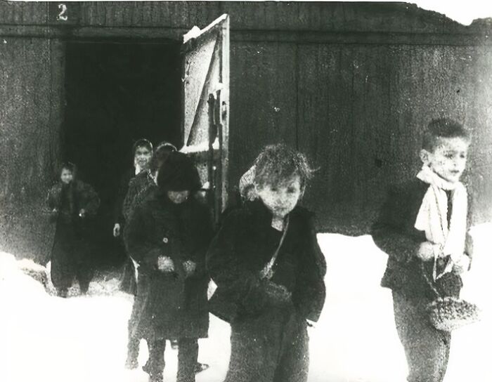 Children dressed in old clothing standing outside a wooden building in the snow, a unique old photo capturing a historical moment.