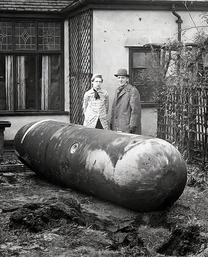 Two people stand outside an old house next to a large unexploded b**b from unique old photos collection.
