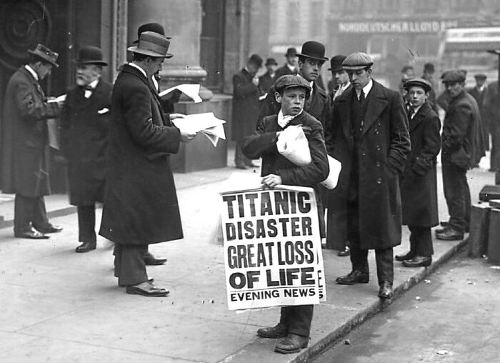Boy selling newspapers with Titanic disaster headline in a rare and interesting historical photograph on a city street.