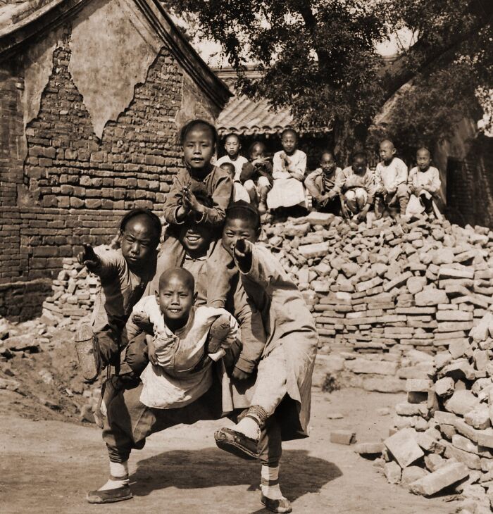 Group of children playing and posing in front of a brick wall in a rare and interesting historical photograph