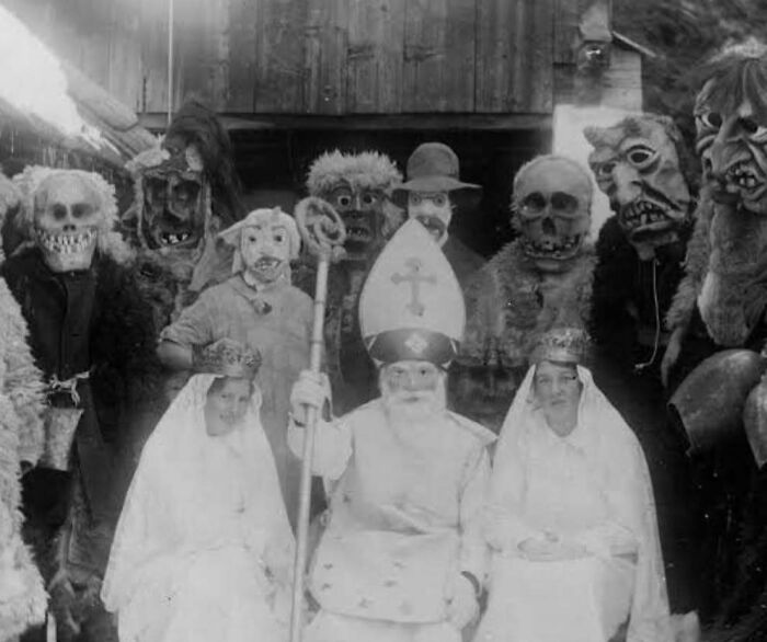 Group of people in vintage scary costumes and masks posing for a black and white photo in a dark setting.