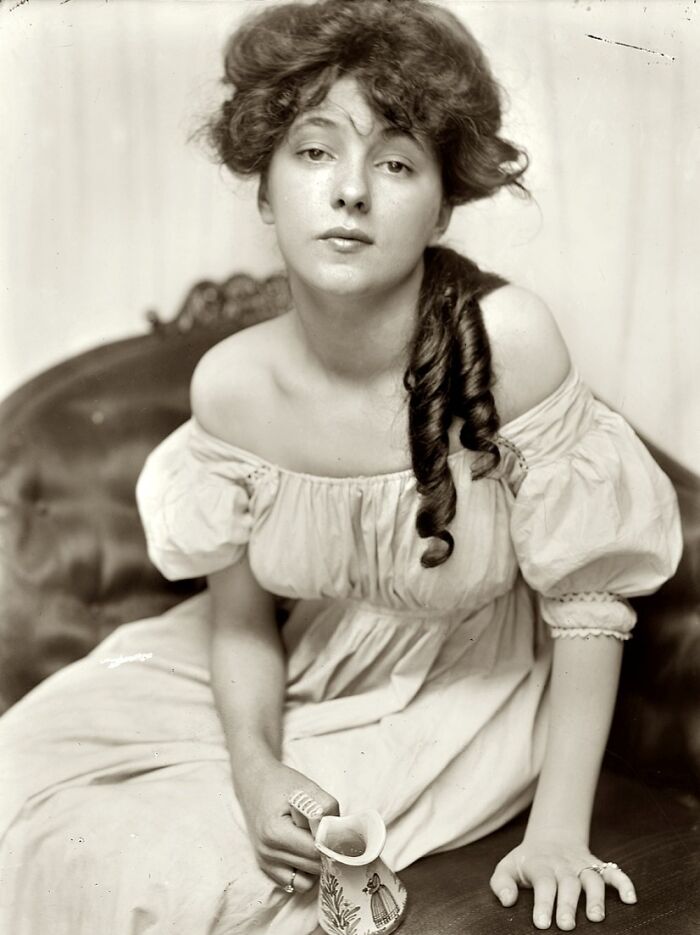 Vintage photo of a woman from the 1900s wearing an off-shoulder dress, showcasing beauty and elegance from the era.