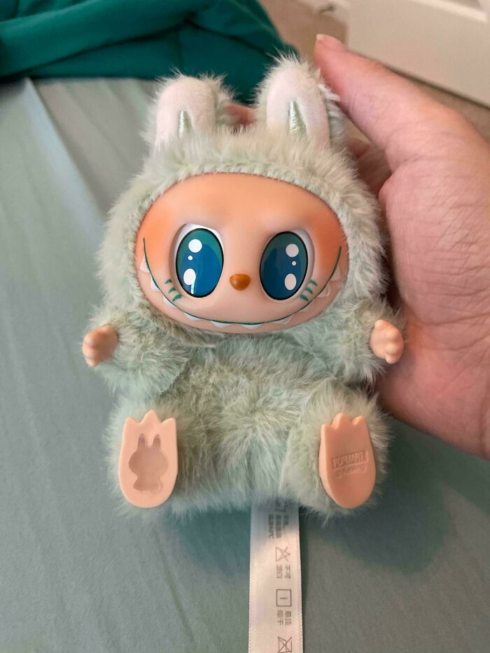 Hand holding a small Labubus doll with large eyes and fuzzy costume, one of the creepy Labubus fakes.