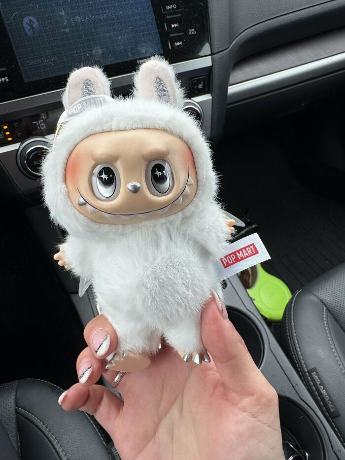 Labubus toy figure in a white furry costume held inside a car, showing creepy and creepy design details.