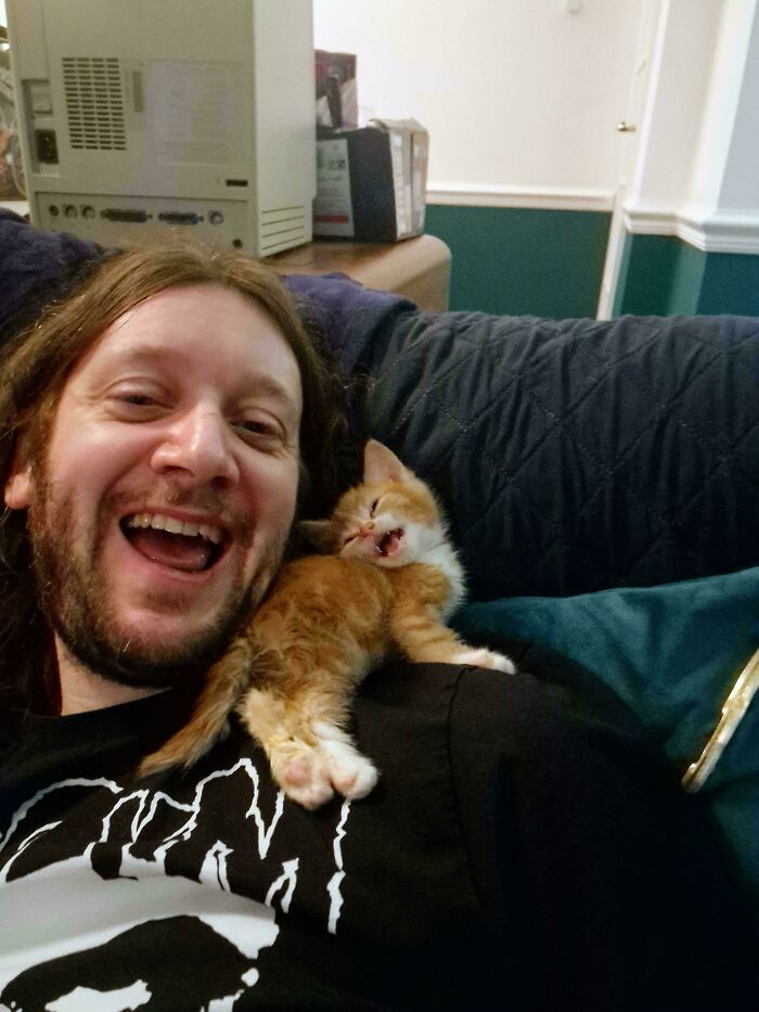 Man laughing with an orange kitten on his shoulder, one of the funny cat moments that made owners laugh and share online.
