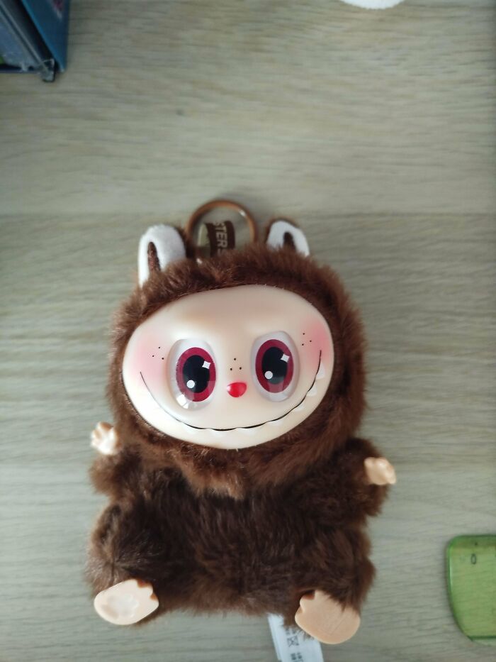 Creepy Labubus fake toy with large eyes and fur, sitting on a wooden surface, evoking eerie and unsettling vibes.
