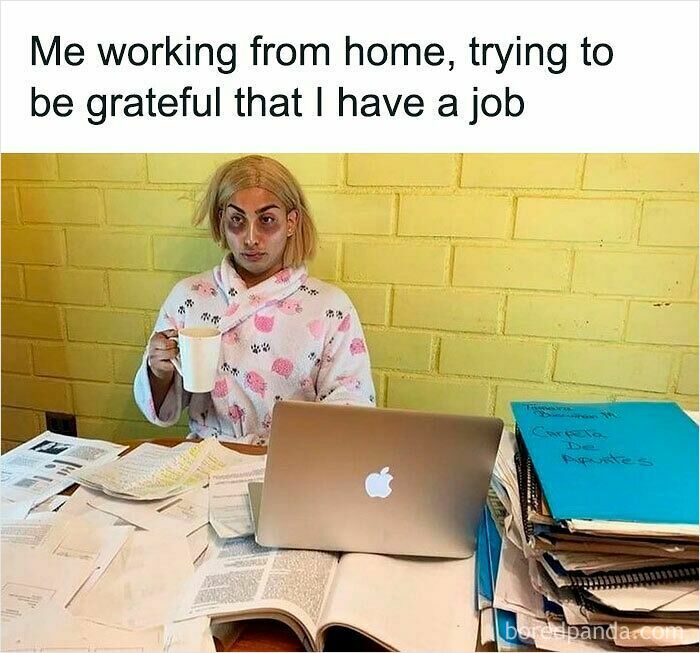 Person in a robe working from home surrounded by piles of papers and a laptop, illustrating funny WFH memes.