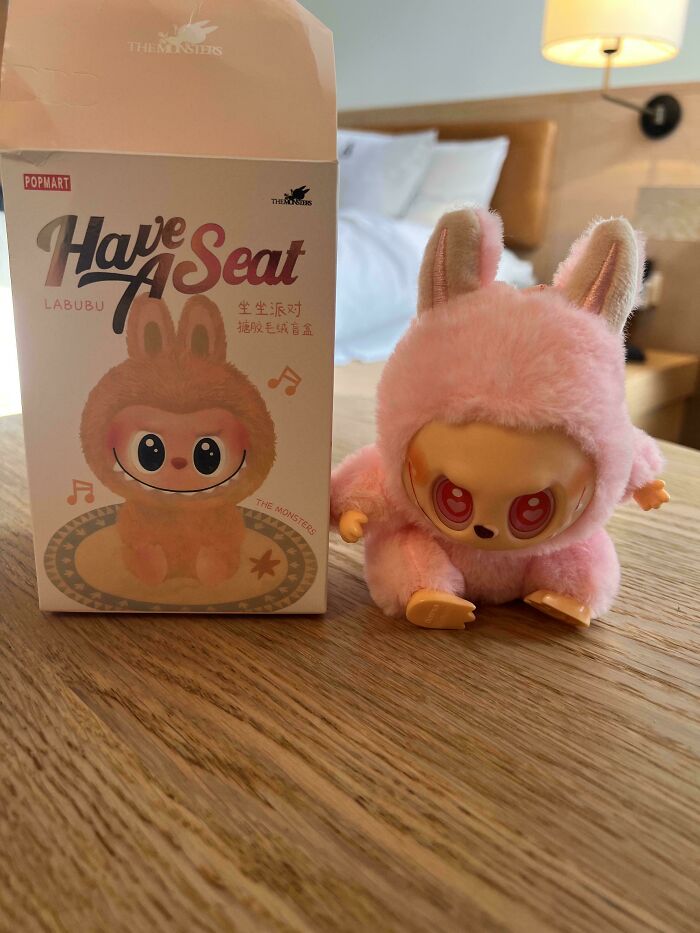 Labubu toy figure in a pink bunny suit next to original packaging, showcasing creepy and unusual design details.