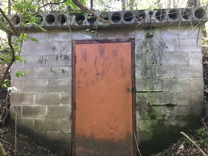 Old concrete structure with a rusted door covered in handprints found in the forest, creepy and terrifying discovery.