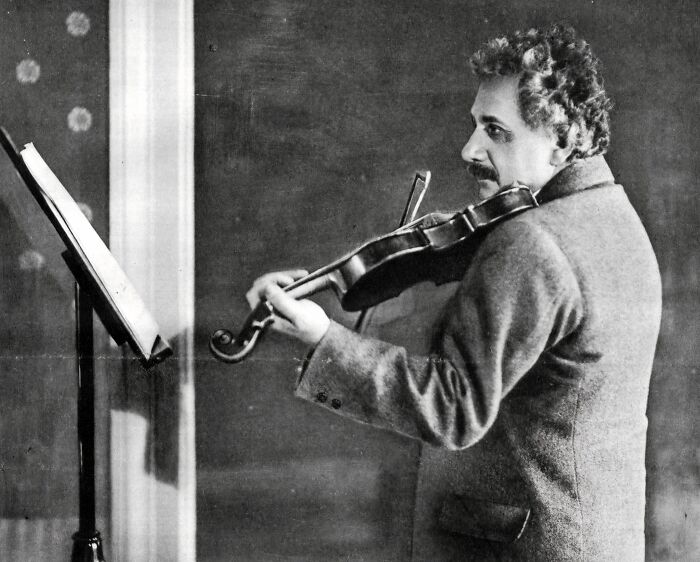 Black and white rare historical photograph of a man playing the violin while reading sheet music on a stand.