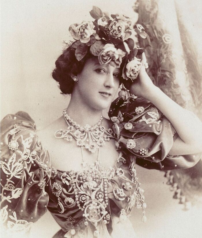 Vintage portrait of a woman adorned with flowers and elaborate jewelry, showcasing timeless beauty from a century-old photo.