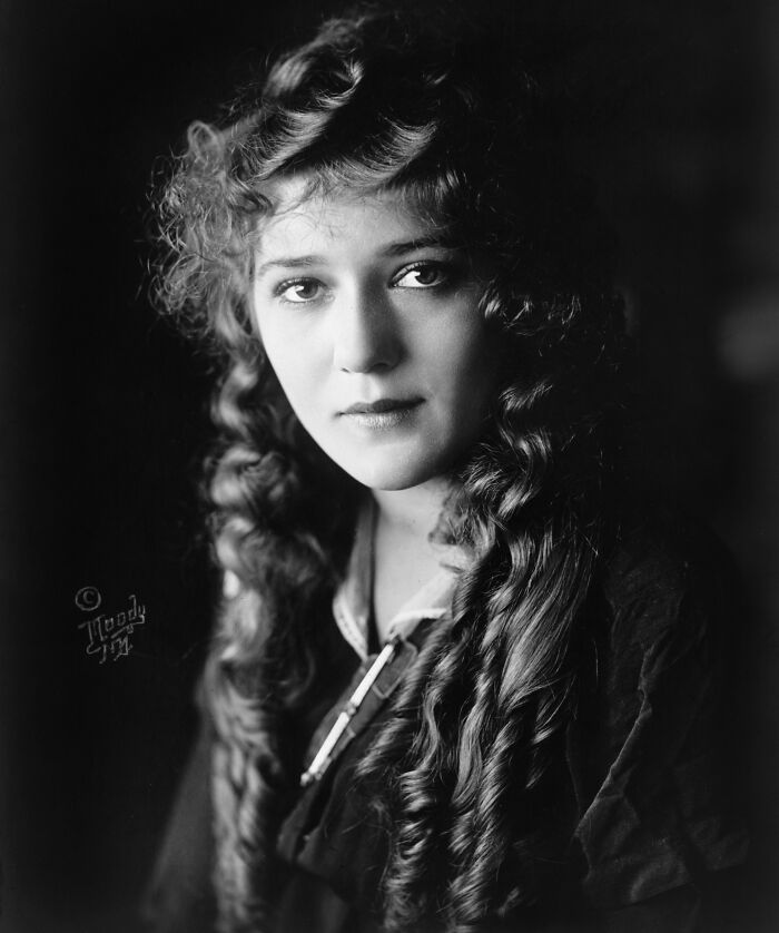 Black and white century-old photo of a woman with long curly hair embodying timeless beauty and classic elegance.