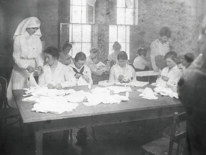Rare historical photograph of nurses and women sewing medical supplies in a wartime hospital room with large windows.