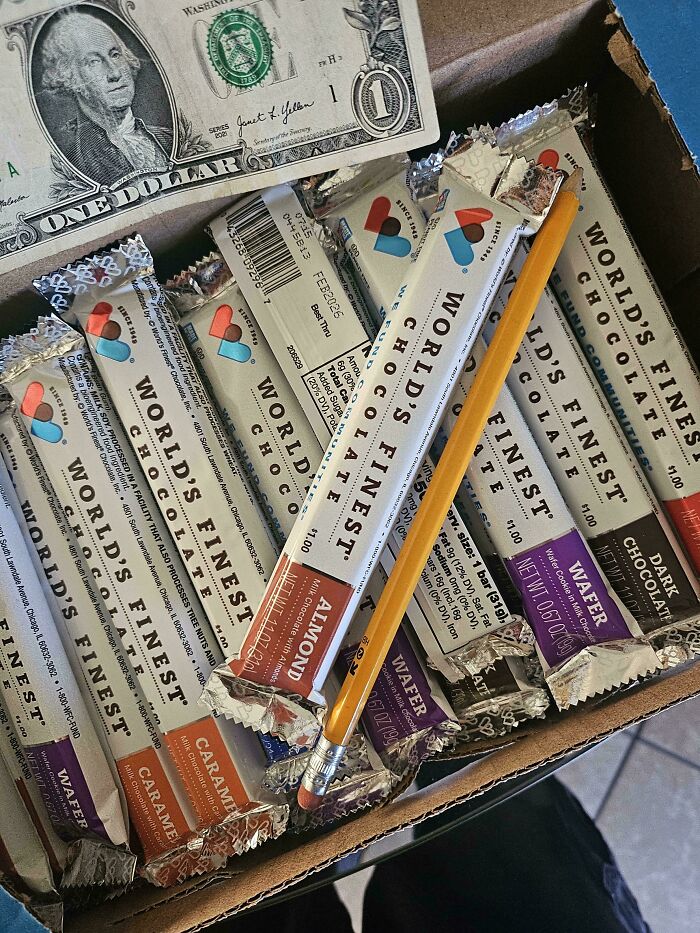 Box of chocolate bars labeled World's Finest with a pencil and a dollar bill, highlighting school fundraising efforts.