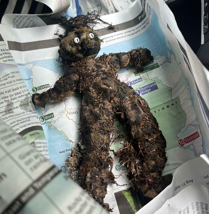 Creepy handmade doll covered in dirt and twigs found in the forest, resting on a folded map inside a bag.