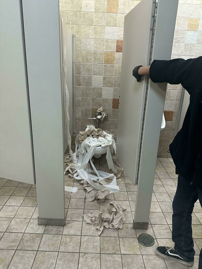 School bathroom stall in disarray with toilet paper strewn everywhere showing schools that are not created equal or great.