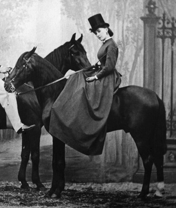 Victorian courtesan dressed in riding attire sitting side-saddle on a horse, representing power players in history.