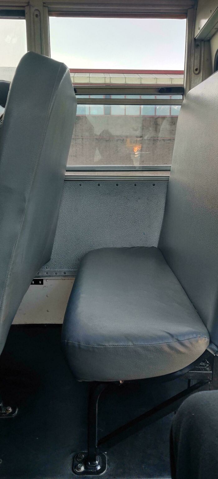 Worn and narrow school bus seat with gray padding inside an older school vehicle, showing school conditions and environment.