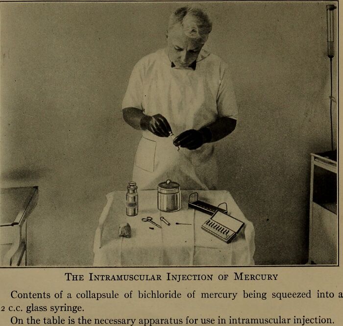 Vintage medical device setup for intramuscular mercury injection by a man in early 20th-century clinical attire.