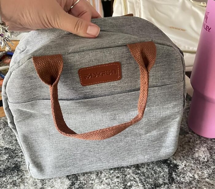 Gray and brown under-the-radar find travel bag held by a hand on a granite countertop with a pink tumbler nearby