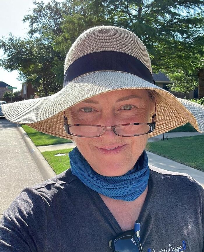 Woman outdoors wearing a large sun hat, glasses, and a neck gaiter, smiling while enjoying camping hacks in nature.