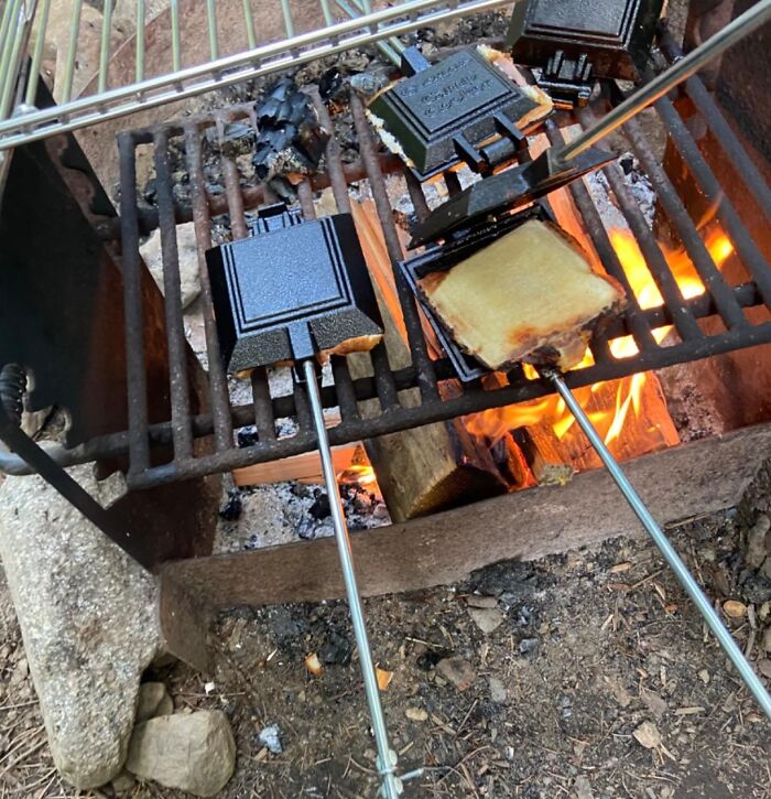 Cast iron sandwich irons grilling toasted sandwiches over an open campfire, showcasing camping hacks for cooking outdoors.