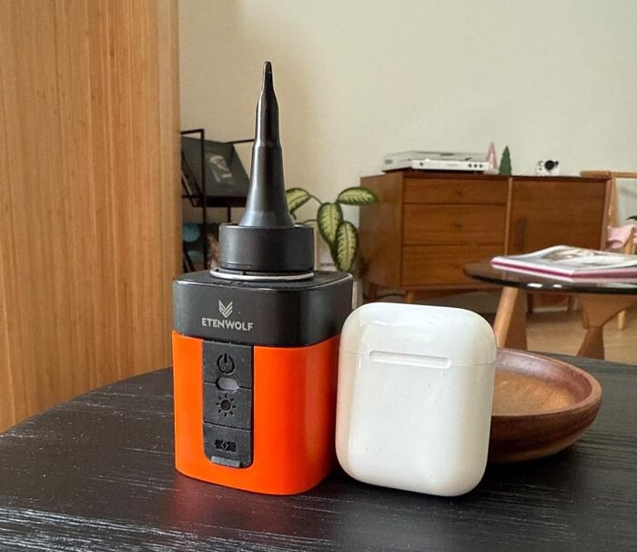 Portable electric air pump for camping gear next to wireless earbuds case on a black table indoors.