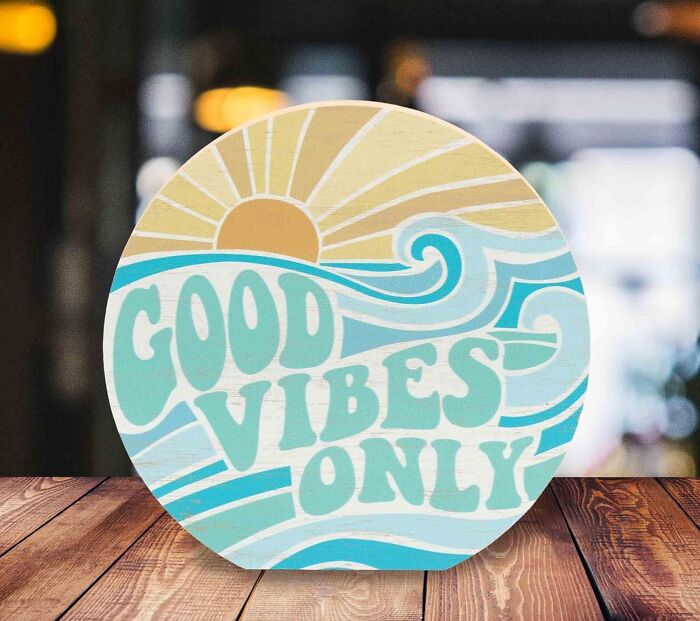 Round wooden sign with sun and waves design displaying good vibes only, an item to create a low-key holiday workspace.