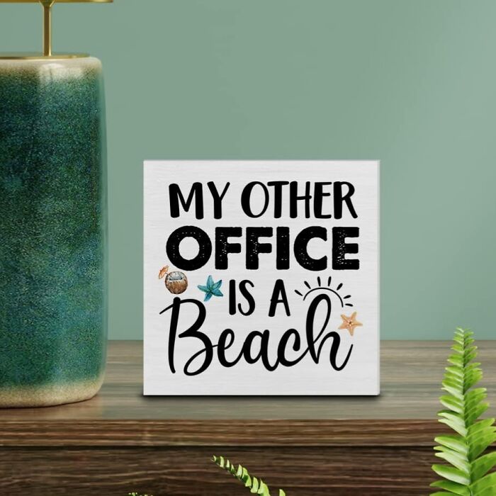 Decorative sign on wooden desk with phrase My Other Office Is A Beach, adding low-key holiday vibe to workspace.