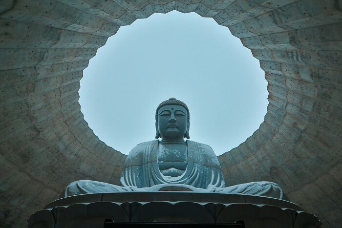 Large Buddha statue viewed from below inside a circular stone structure under a bright sky, addressing religious myths about Jesus.