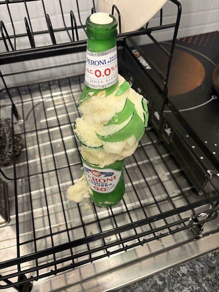 Frozen broken beer bottle inside a dishwasher rack showing a funny unfortunate situation of forgetting to remove it before washing.