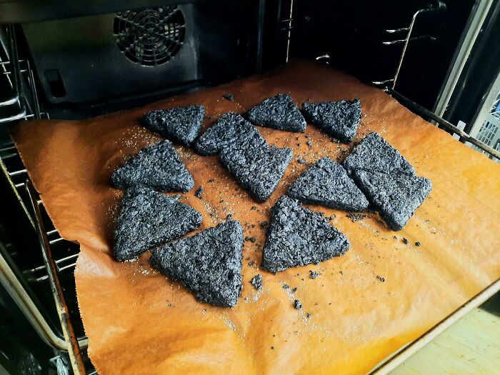Burnt triangular snacks inside an oven on parchment paper, showing a funny unfortunate situation of forgetting food.