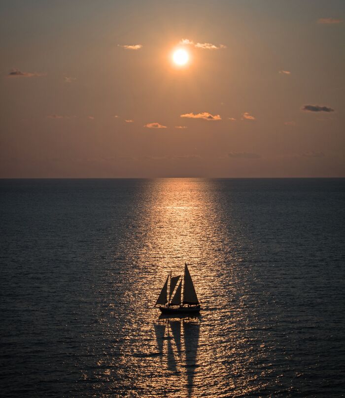 Sailboat sailing into the sunset on calm water, capturing an amazing moment of unbelievable luck and peaceful beauty.