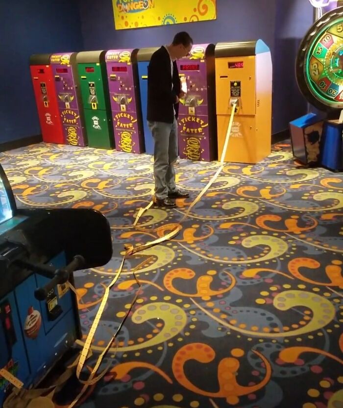 Man experiencing unbelievable luck collecting an extremely long ticket from arcade machines inside a colorful game room.